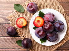 Ripe Whole Plums And Half In A Plate On A Wooden Background. The View From Top