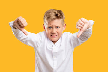 Dislike gesture. Awful idea. Dissatisfied boy in white shirt showing thumbs down isolated on orange.