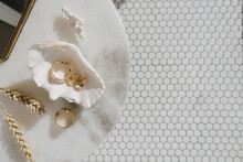 Minimal Fashion Composition With Golden Earrings In Seashell On Marble Table With Mirror And Wheat Stalks. Flat Lay, Top View Bijouterie / Jewelry Concept On Mosaic Tile Background.