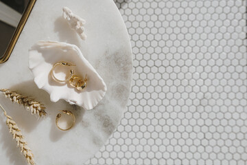 minimal fashion composition with golden earrings in seashell on marble table with mirror and wheat s