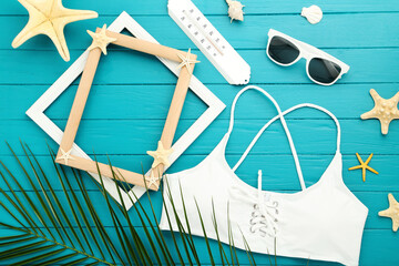 Wall Mural - Fashion swimsuit with palm leaf, sunglasses, starfishes, thermometer and photo frames on blue wooden table