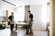 © Svitlana - Moving your home. Full length shot of two contractor employees, young and aged repairmen in uniform moving personal belongings, table in the kitchen. Service concept