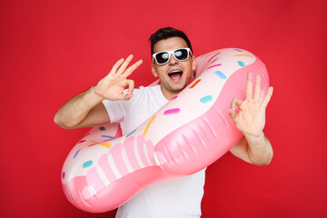 Young man with inflatable donut showing gesture Ok on red background