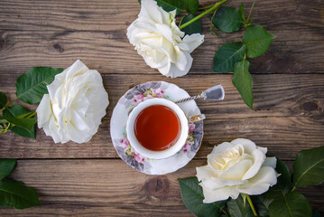 Canvas Print - White roses and a cup of tea on a wooden background