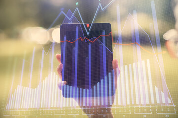 Double exposure of forex chart sketch hologram and woman holding and using a mobile device. Financial market concept.