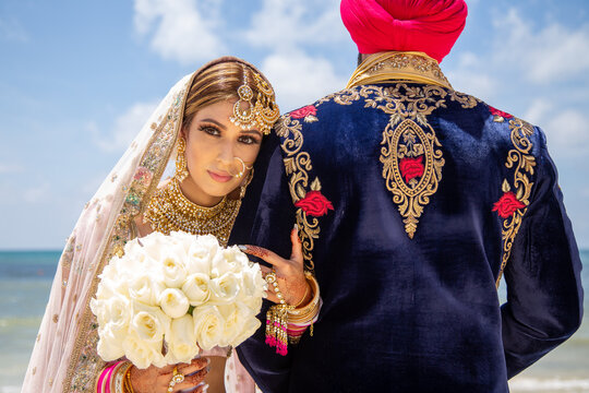 Sikh bride and groom wearing bright traditional clothing on clear sandy beach beneath sunny blue skies