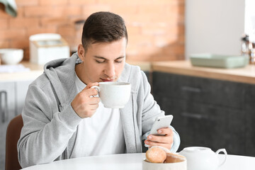 Wall Mural - Handsome young man with mobile phone drinking tea at home