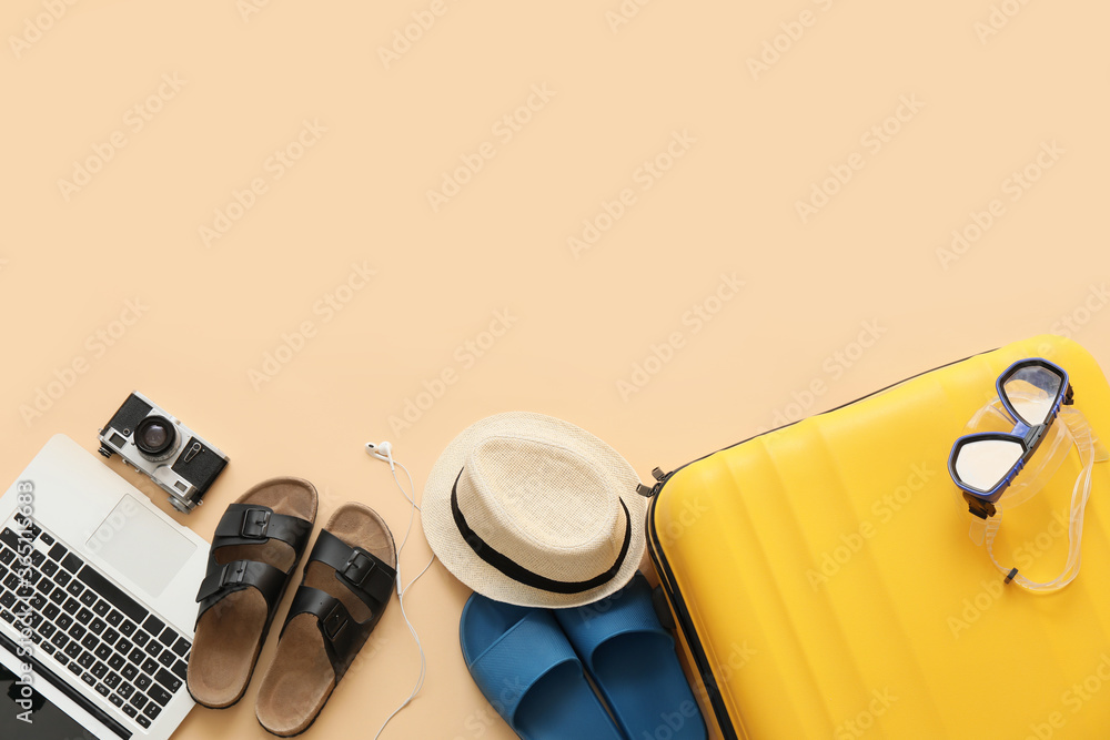 Suitcase with beach accessories and laptop on color background