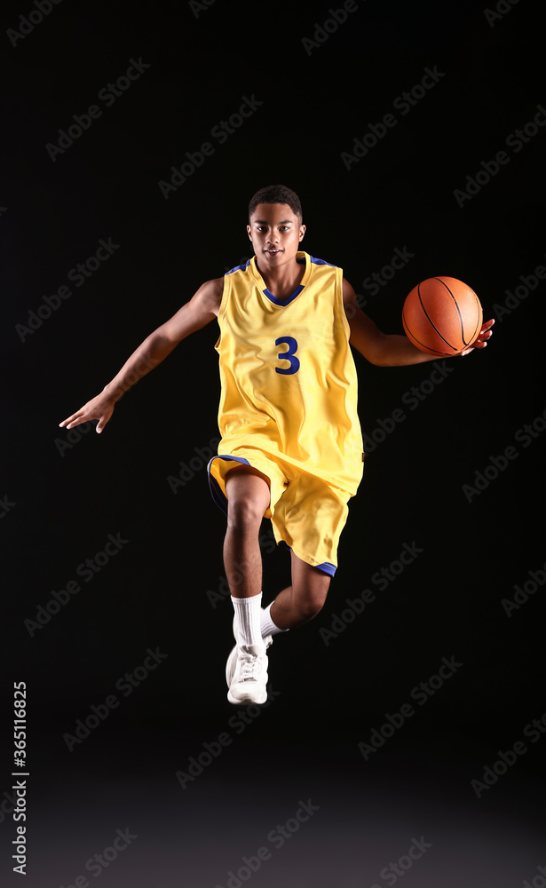 Young jumping African-American basketball player on dark background