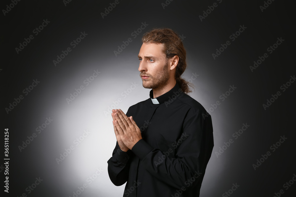 Handsome praying priest on dark background