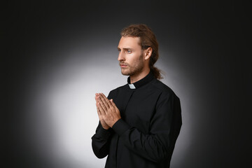 Wall Mural - Handsome praying priest on dark background