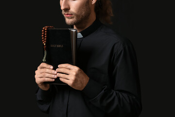 Wall Mural - Handsome priest with Bible on dark background