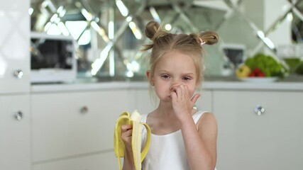 Sticker - Child Eating Food. Little Girl Eating Banana At Kitchen. Portrait Of Cute Kid With Fruit In Hand 