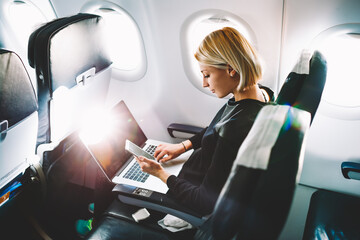 blonde female tourist checking incoming notification on smartphone sitting on seat of airplane with 