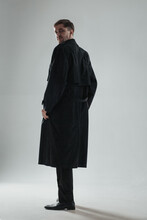 Mysterious man turned back to camera in a long dark trench coat. Vertical image.