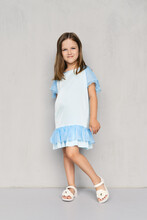 Cute Little Girl In Blue Dress And Sandals Posing Near The Wall