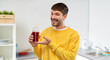 © Syda Productions - drinks and people concept - happy smiling young man holding tomato juice in takeaway plastic cup with paper straw over home kitchen background