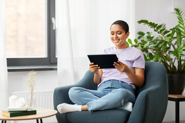 people, technology and leisure concept - happy young african american woman with tablet pc computer sitting in chair at home