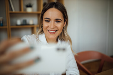 Wall Mural - Portrait of a happy young woman taking selfie indoors.