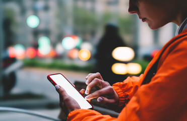 Close up view of female person using smartphone app for online shopping. Woman's hands holding mobile phone with big copy space touch screen outdoors with evening bokeh light of city on background.