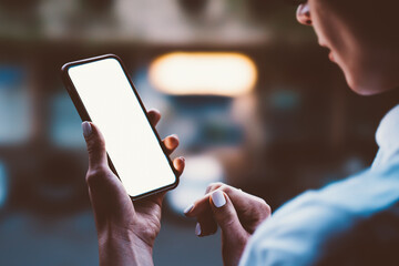 woman's hands holding mobile phone with lighted big copy space touch screen outdoors with evening bo