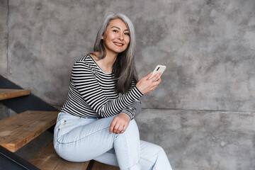 Canvas Print - Photo of happy adult asian woman smiling and using cellphone