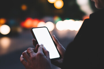 Cropped view of young woman holding smartphone with blank screen area for your internet content on bokeh background.Female finger typing text on website on digital mobile phone using 4G connection