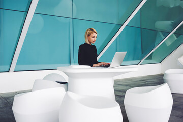 Creative woman designer developing new project on laptop computer before important meeting with employer, confident copywriter preparing promotional materials while sitting in modern office interior