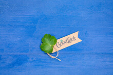 Tag With Text “Good Luck” And Fresh Green Clover Leaf Are On The Centre Of Creative Blue Wooden Background, Copy Space For Your Ideas. Flat Lay Composition Top View.