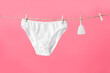 Menstrual cup and women's underwear hanging on clothesline isolated on pink background, poster for women's blog or ad 