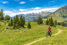 Active Senior Woman Riding Her Electric Mountain Bike Below The Seven Summits Of Churfirsten In Canton St. Gallen, Switzerland, Landscape