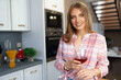 © fotofabrika - Blonde caucasian woman with glass of red wine standing in her kitchen