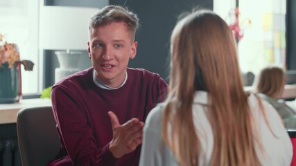 Wall Mural - Serious confident gen-z young male freelancer talks to blonde female colleague at modern busy light office table meeting