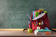 © Davizro Photography - Backpack full of school supplies on table and blackboard front