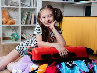 a cheerful girl leaned on a red suitcase that does not close because of a large number of things. op