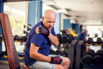 A portrait of senior man feeling strong shoulder pain during training in the gym. People, healthcare and lifestyle concept