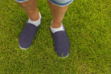 Close up view of male feet in black sneakers on green grass lawn on sunny day. Summer men shoes.