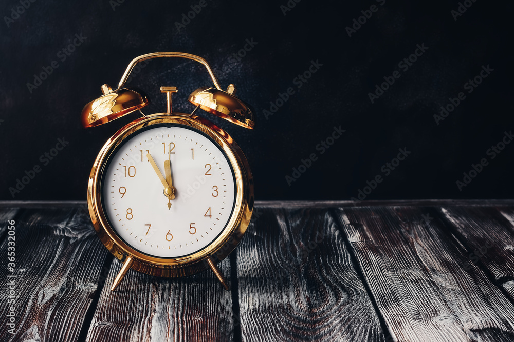 Gold alarm clock on a vintage wooden dark table. Rustic style. Selective focus, copy space. Time five minutes to twelve. - obrazy, fototapety, plakaty 