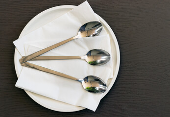 Top view of three spoons on a plate with napkins on a table.