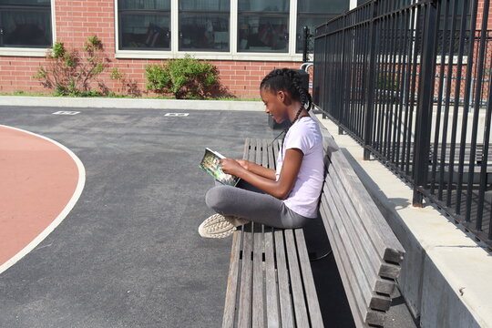 Girl sitting on a park bench reading a book far shot