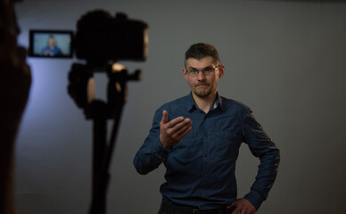 professional actor plays role of confused man and raises hand in front of blurry black camera on tripod close view