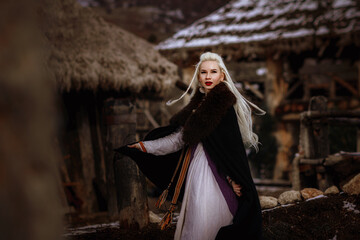 Beautiful blonde Viking dressed in a black cloak against the backdrop of the castle