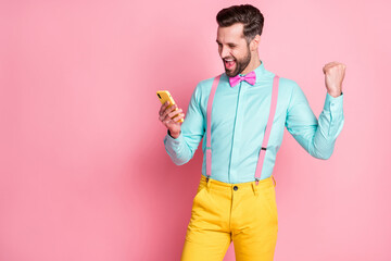 Sticker - Portrait of ecstatic crazy man use smartphone blogging win social network lottery raise fists scream yes wear yellow pants trousers shirt isolated over pastel color background