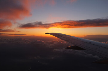 Spectacular sunset from inside an airplane over clouds a valley and a river with the left plane wing visible and the horizon mid frame.