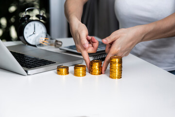 Savings, woman hand stacking gold coins into increasing columns at table office.