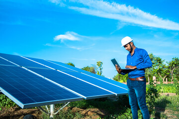 Young male engineer with laptop in hand standing near solar panels, agriculture farm land with clear blue sky background, Renewable energy, clean energy.