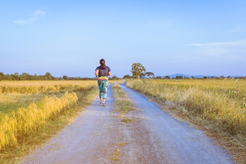 Wall Mural - Back view of woman running and exercising on the path through the rice fields in the evening.