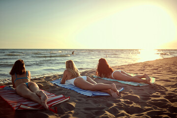 Wall Mural - three young attractive females laying down on the beach, enjoying the sunset. copy space