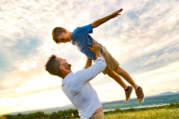 Wall Mural - happy family of father and child on field at the sunset having fun flying in the air