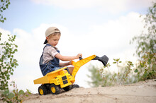 Child, Little Boy Have Fun With Toy Excavator And Dumper In The Sand. Carefree Childhood.
